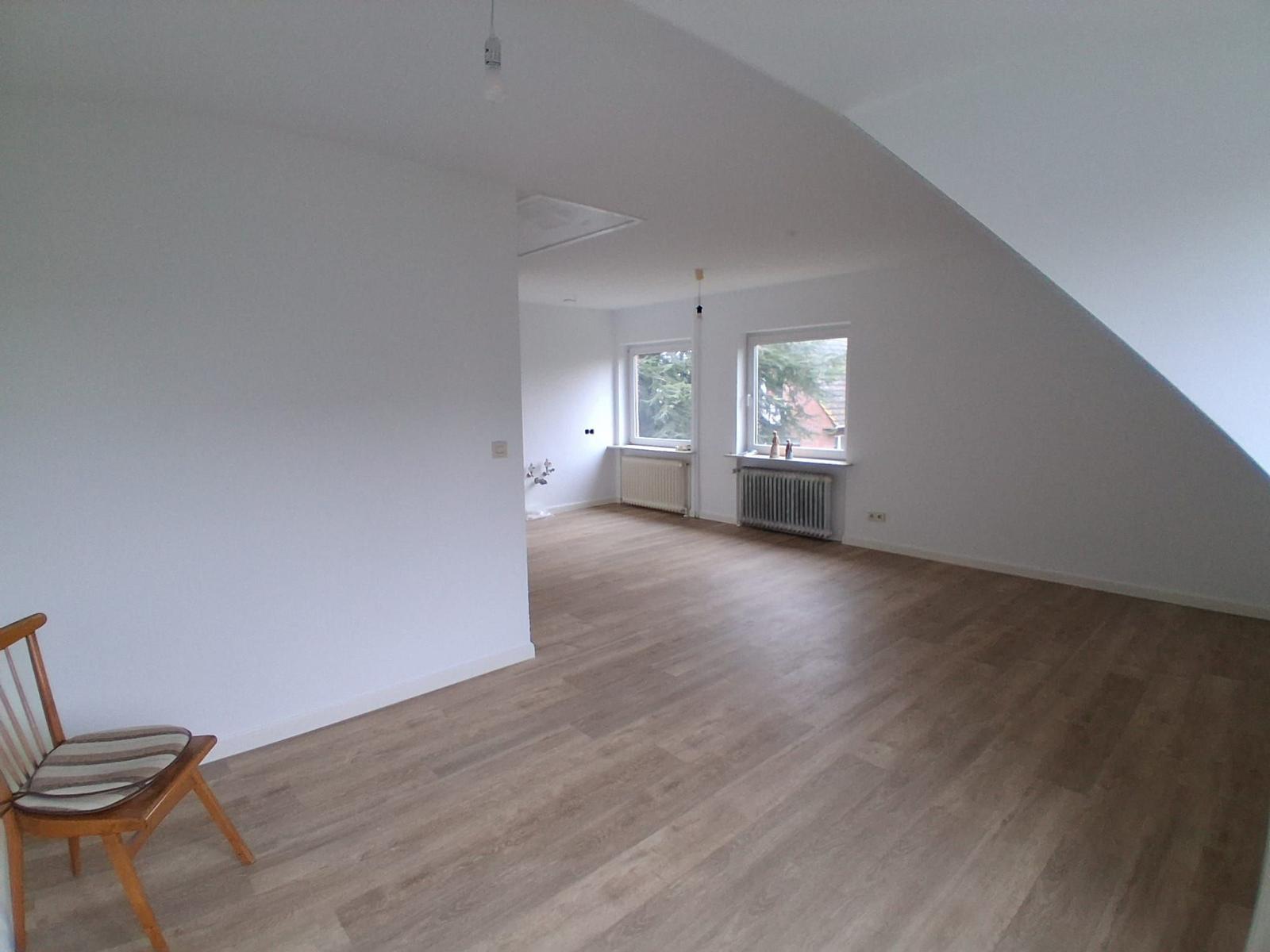 Großes Zimmer mit Holzboden und Dachschräge. Fenster mit Blick nach außen.