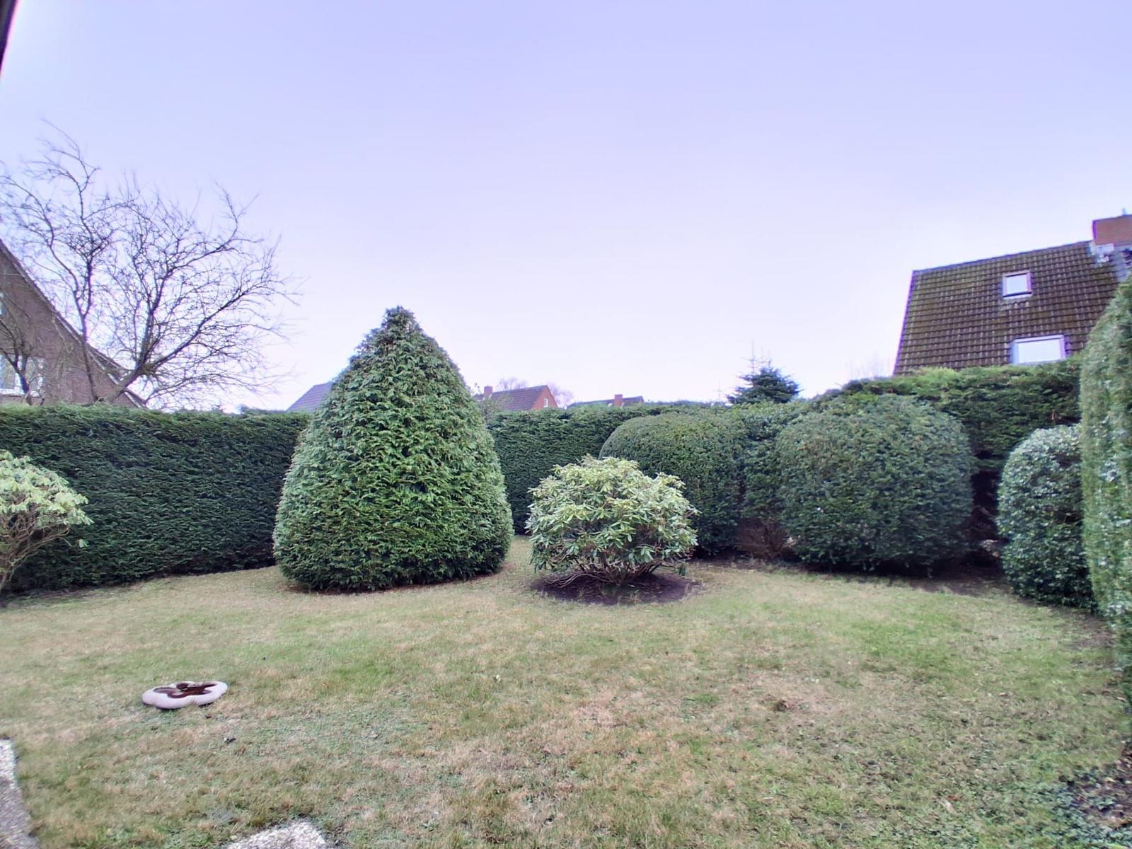 Garten mit Rasenfläche und gestutzten Hecken sowie Bäumen.