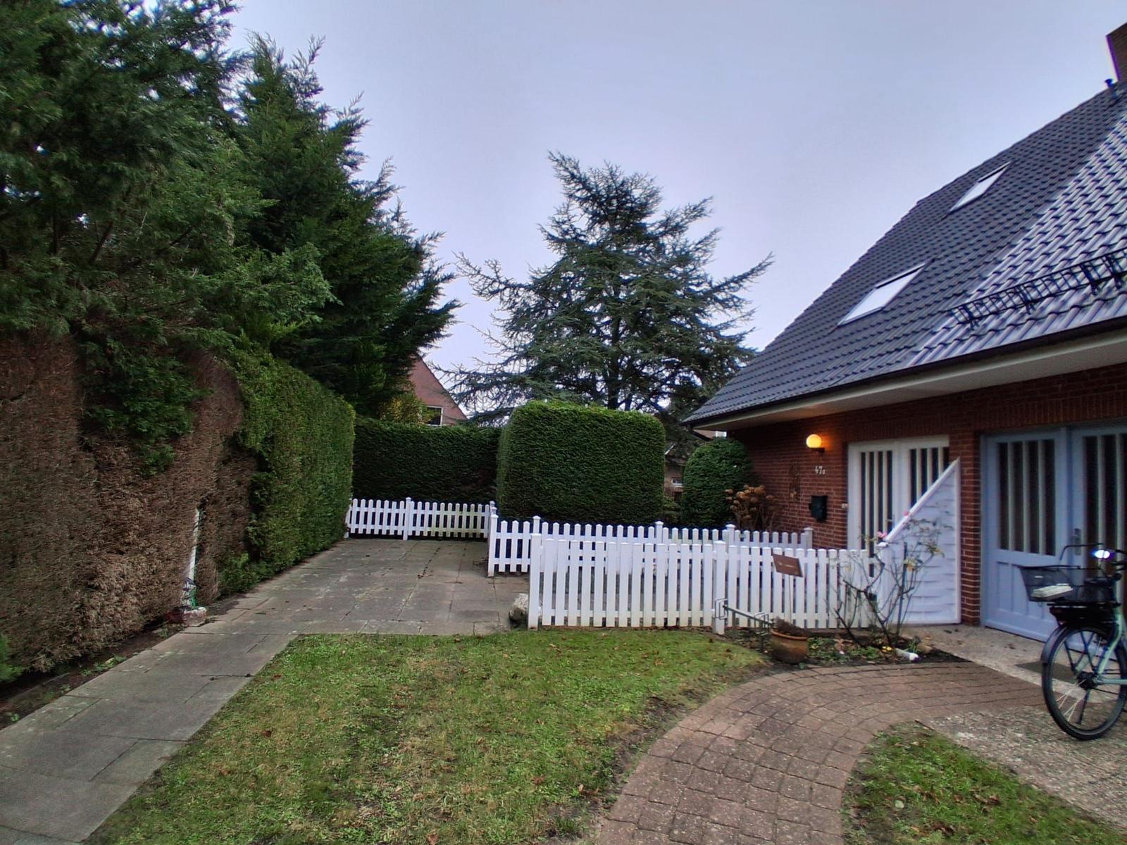 Haus mit weißen Zaun, Rasen und gepflastertem Weg. Fahrrad steht vor der Garage.