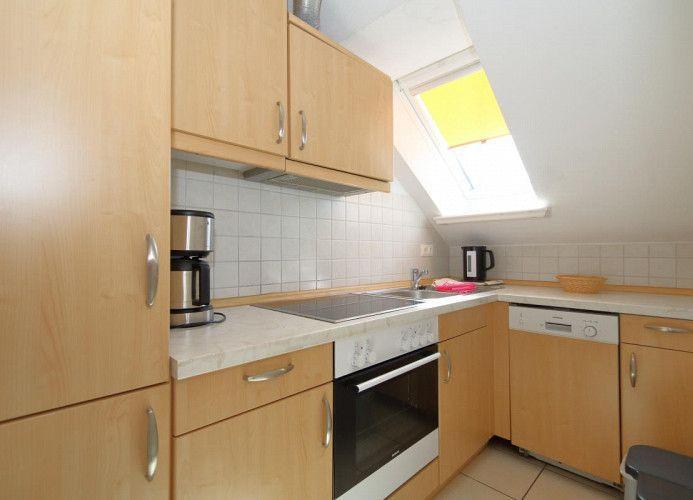 Küche mit Holzschränken, Spüle, Kochfeld und Waschmaschine unter Dachschrägen