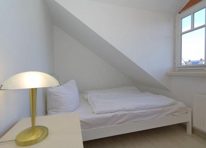 Schlafzimmer mit Dachschräge, Fenster und Nachttisch mit Lampe.