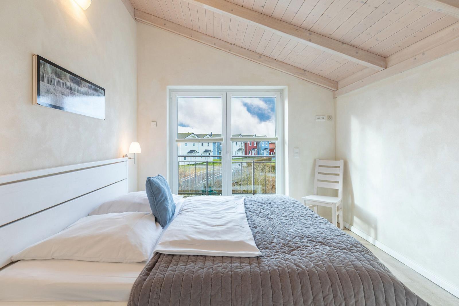 Schlafzimmer mit Bett, Fenster und Stuhl. Blick auf Außenbereich.