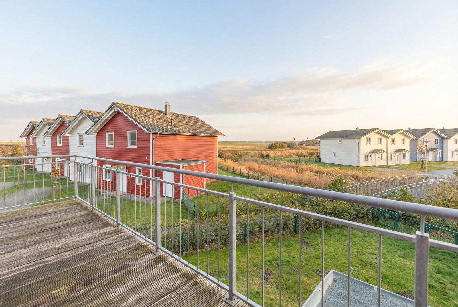Terrasse mit Blick auf rote und weiße Häuser und Grünflächen.