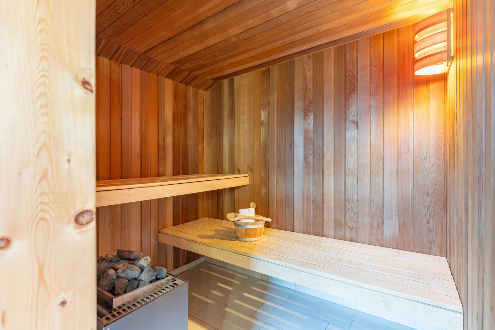 Sauna mit Holzwand, Sitzbank und Körbchen mit Holzlöffel.