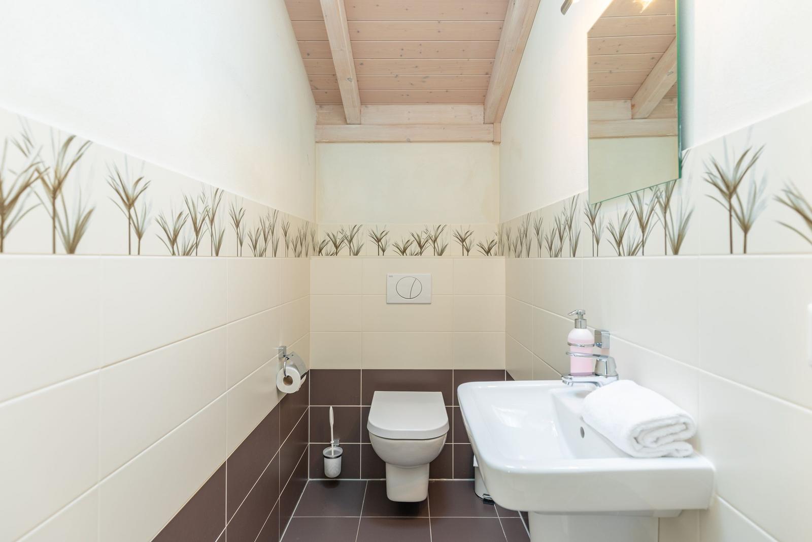 Badezimmer mit Toilette, Waschbecken und Spiegel. Holzdecke und Pflanzenmuster an den Wänden.