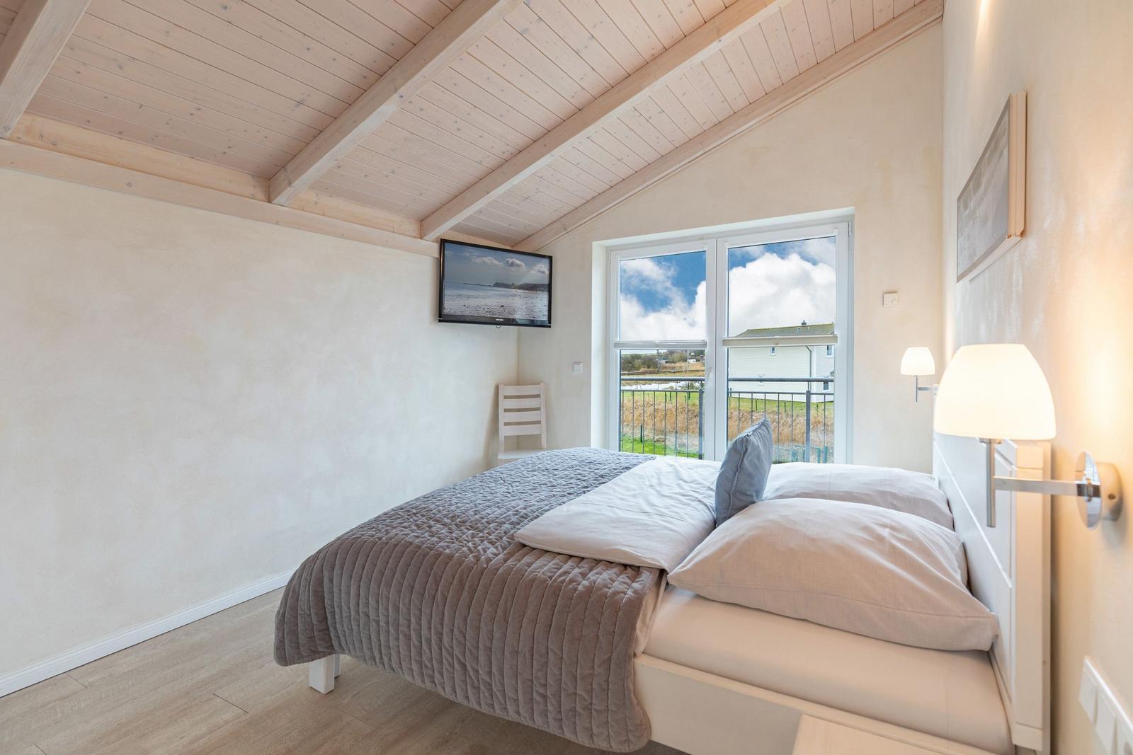 Schlafzimmer mit Bett, TV und Fenster zum Balkon.