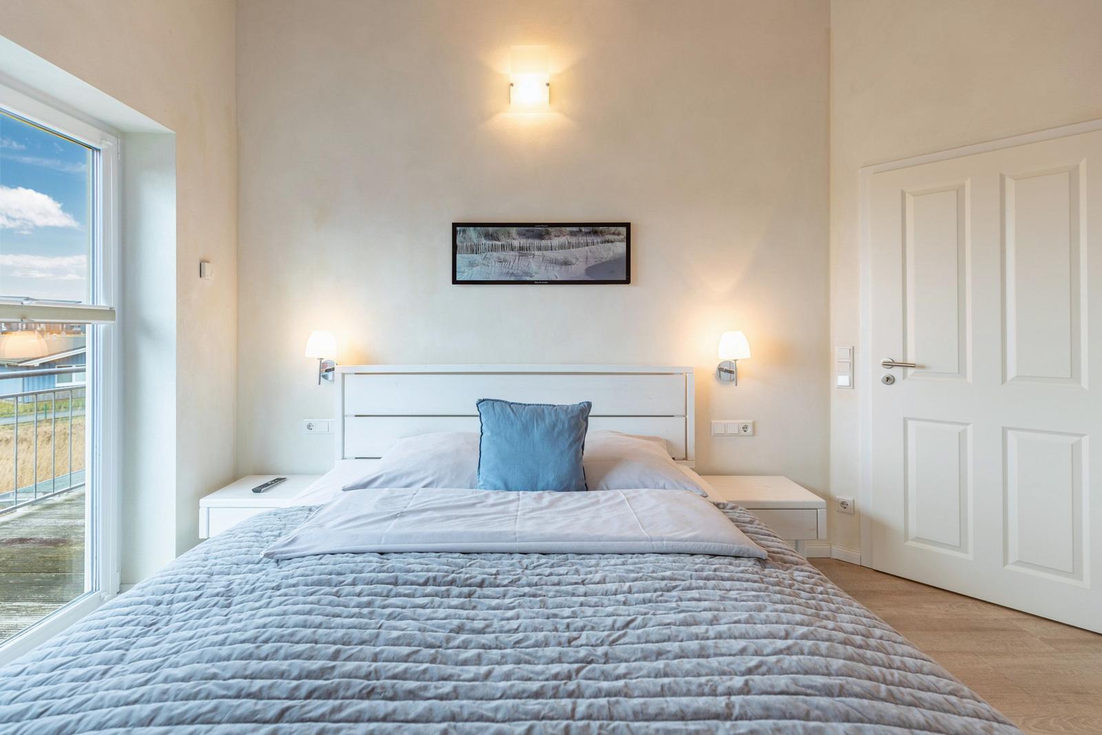 Schlafzimmer mit Bett, Nachttischen und Fenster zur Terrasse.