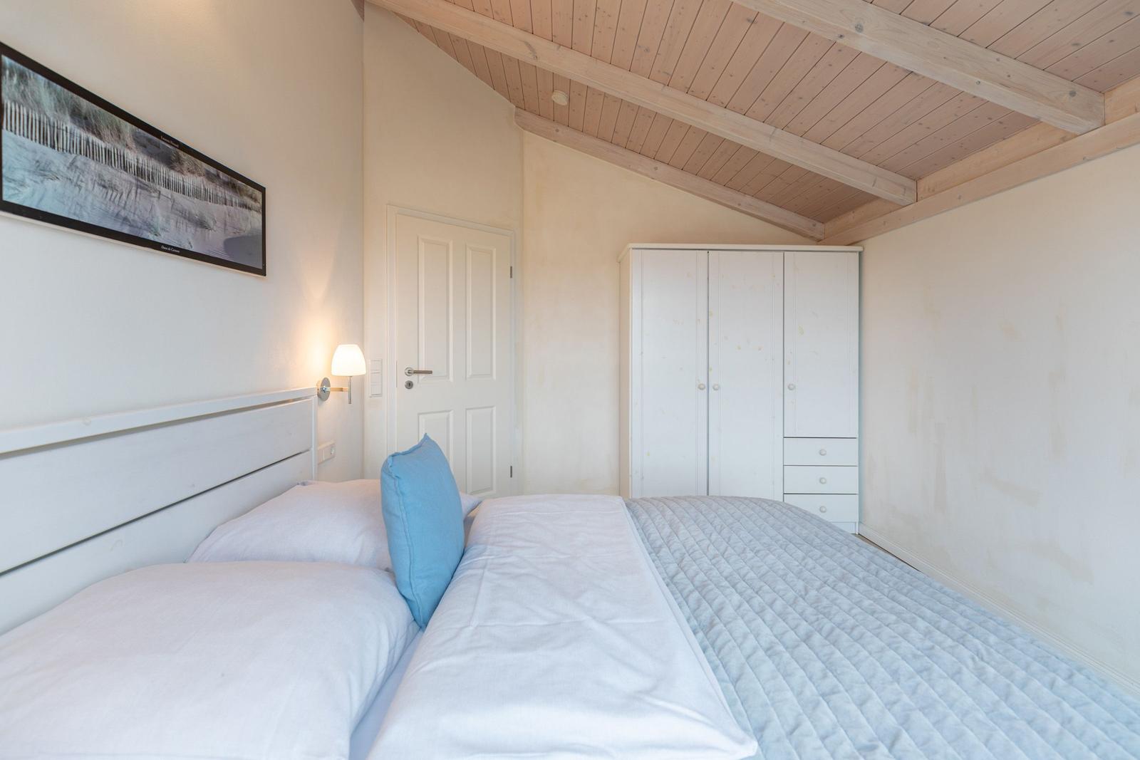 Schlafzimmer mit Doppelbett, Kleiderschrank und Holzdecke.