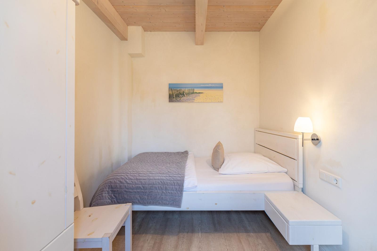 Schlafzimmer mit Bett, Wandlampe und Bild an der Wand.