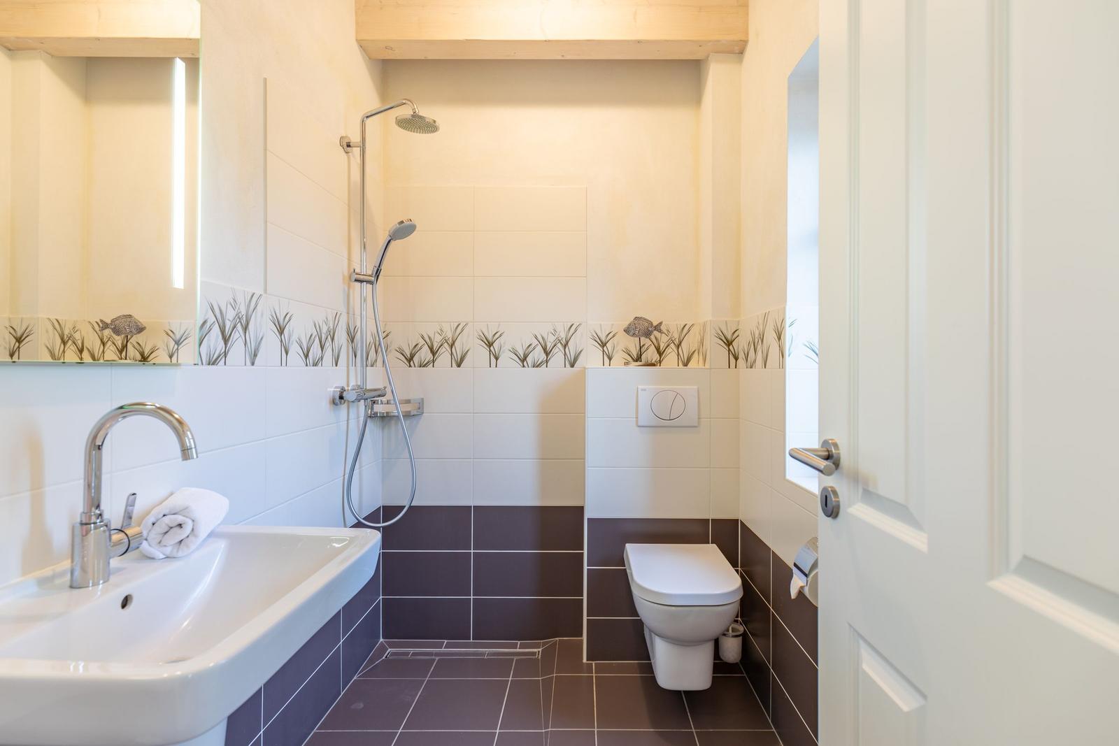 Badezimmer mit Dusche, Waschbecken und Toilette. Fliesen und Spiegel mit Fischmotiv.