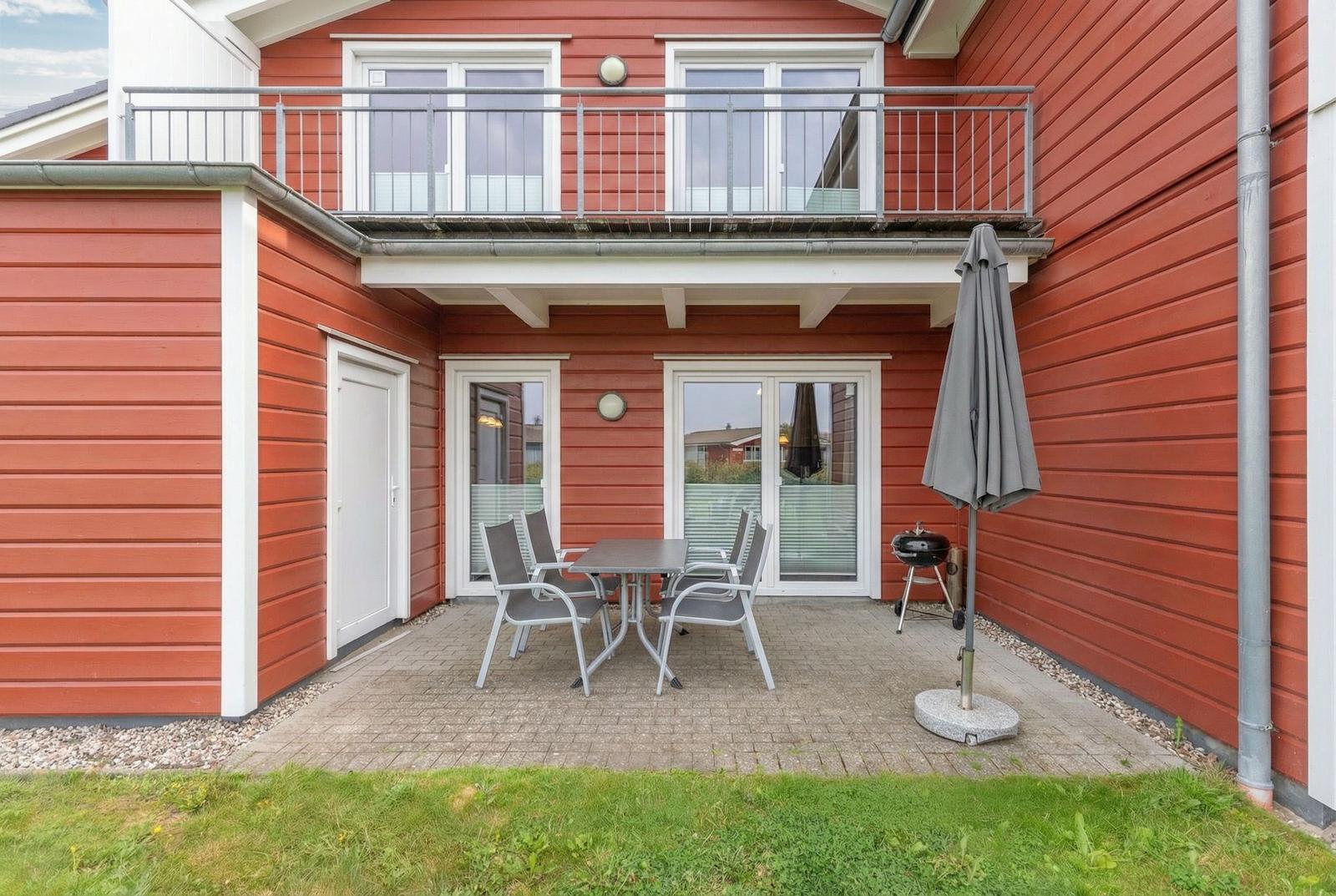Roter Holzhaus mit Balkon, Terrasse, Tisch, Stühlen und Grill.