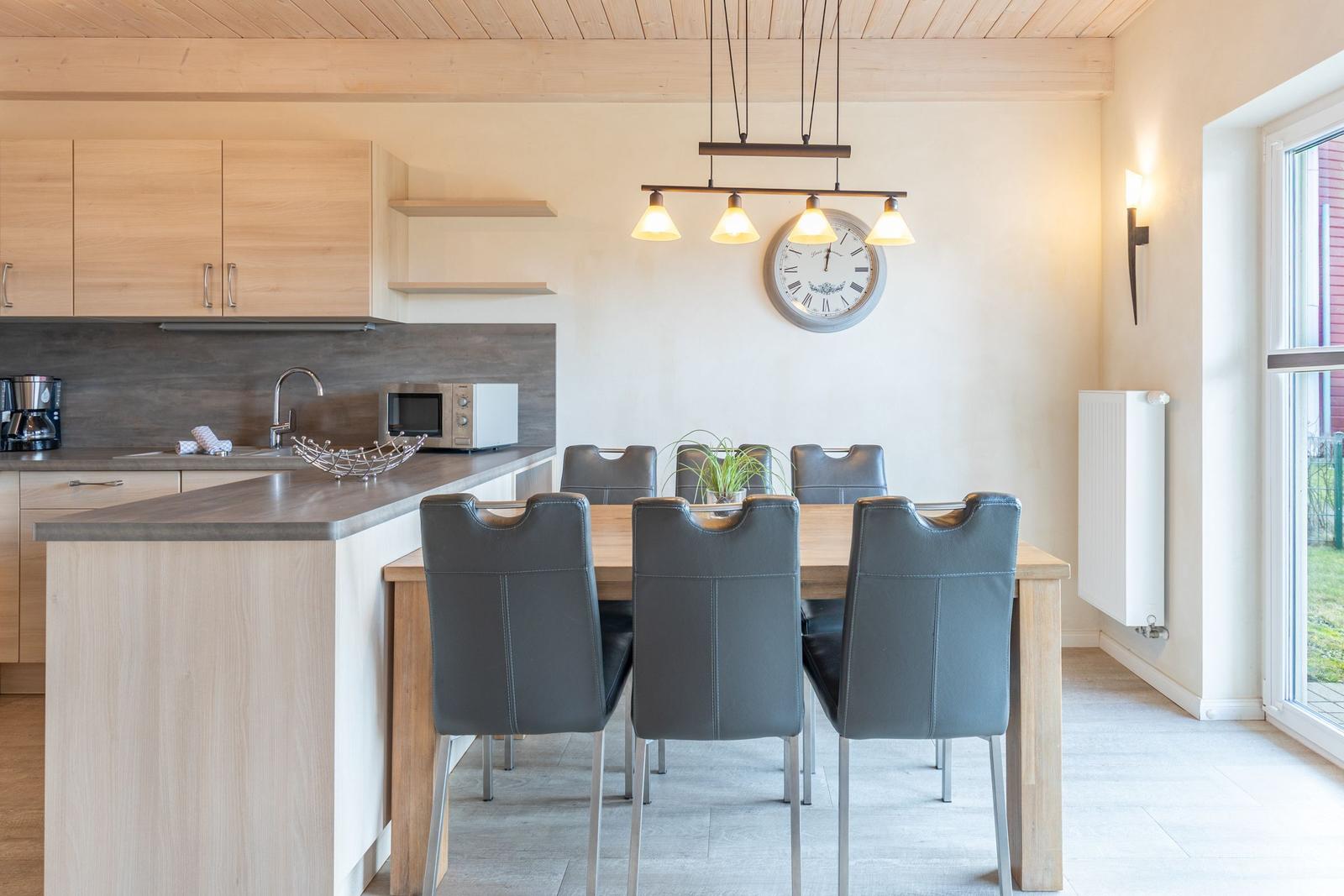 Küche mit Essbereich, Holztisch, grauen Stühlen und Deckenleuchte.