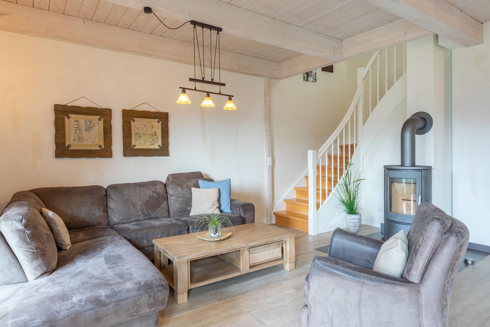 Wohnzimmer mit Sofa, Sessel und Holztisch. Hintergrund: Treppe und Kaminofen.