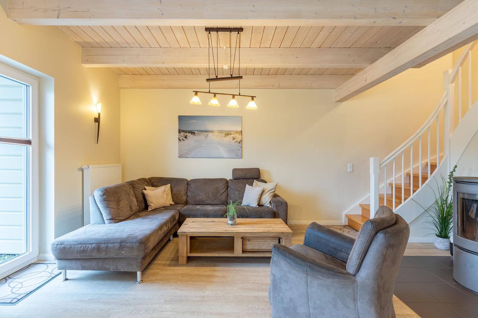 Wohnzimmer mit Sofa, Sessel und Holztisch unter Holzbalkendecke.