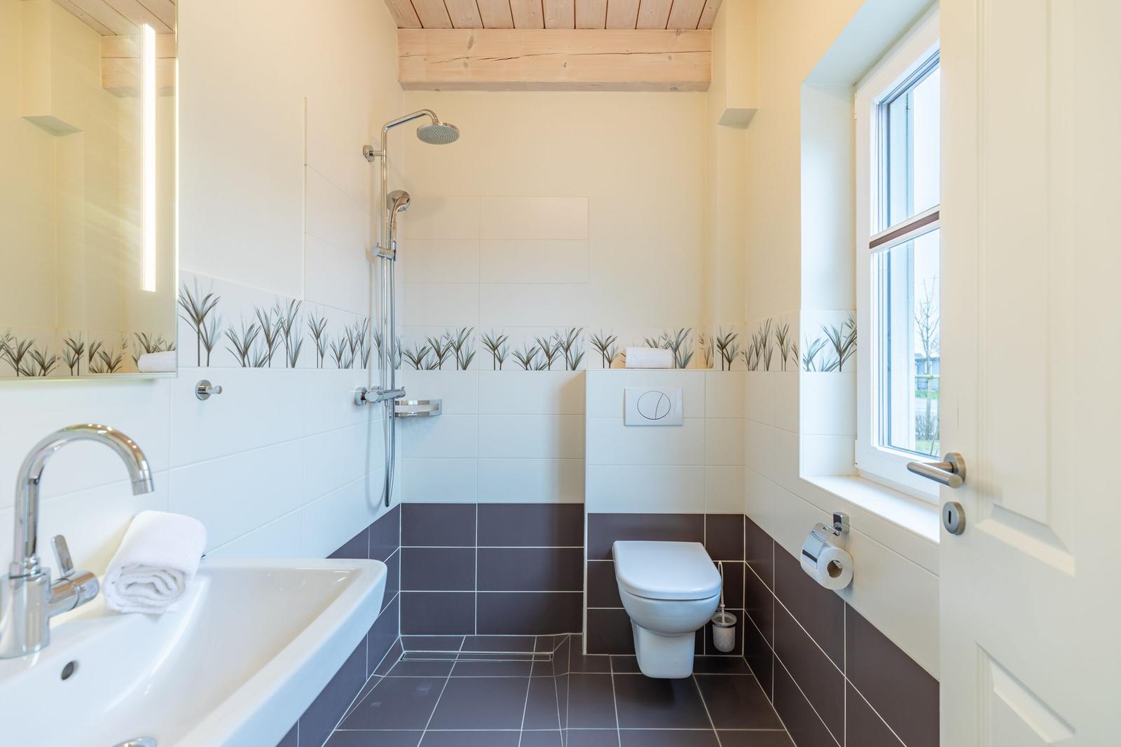 Badezimmer mit Dusche, Toilette und Waschbecken. Holzdecke und Fenster.