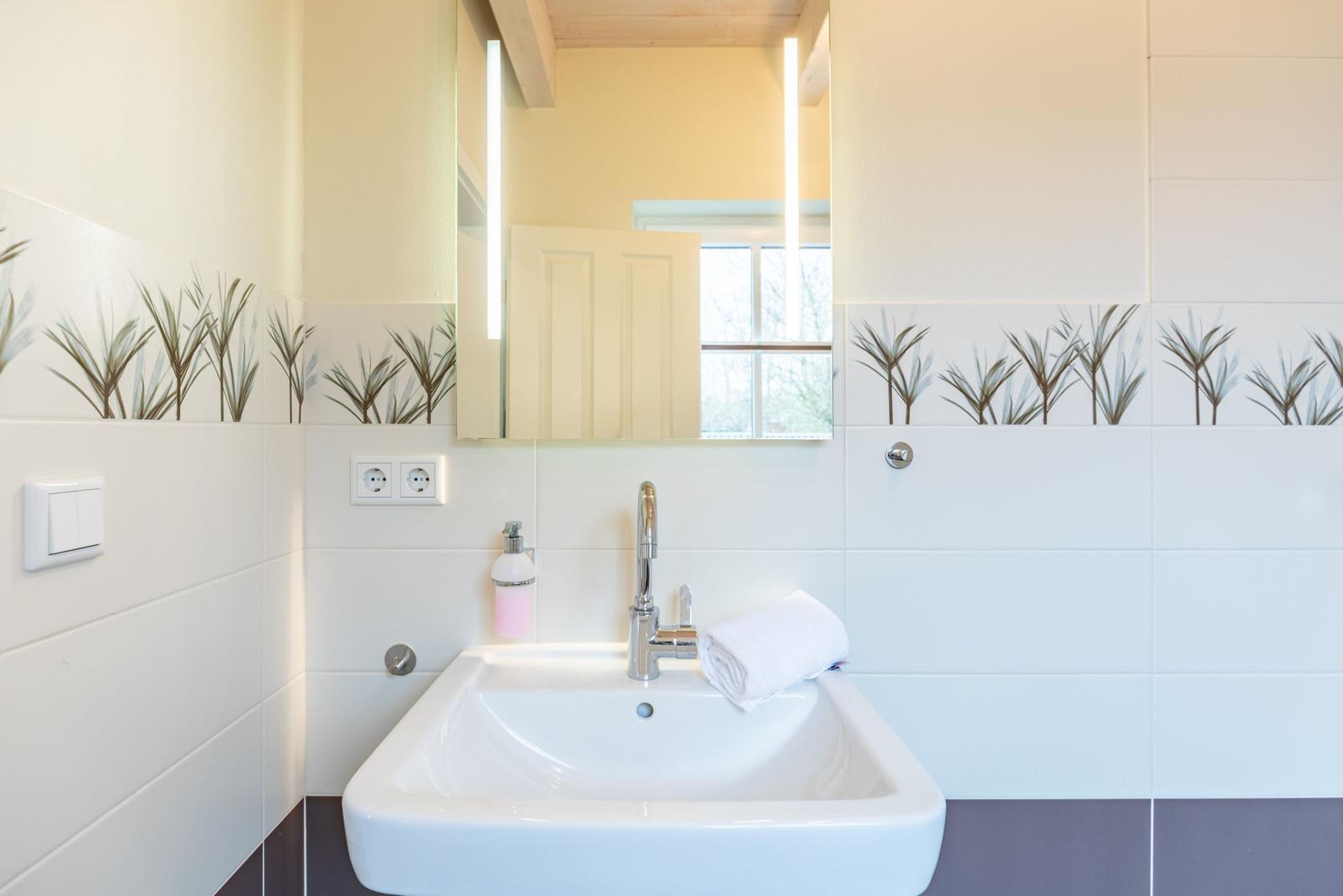 Badezimmer mit Waschbecken, Spiegel und Pflanzenmotivfliesen