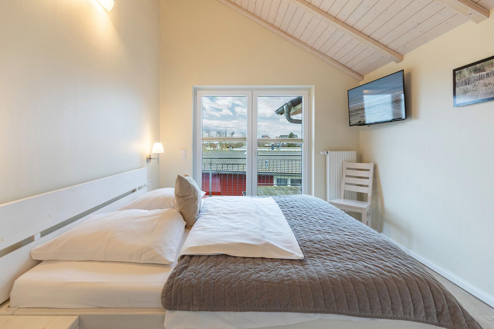 Schlafzimmer mit Bett, Fernseher und Balkontür.