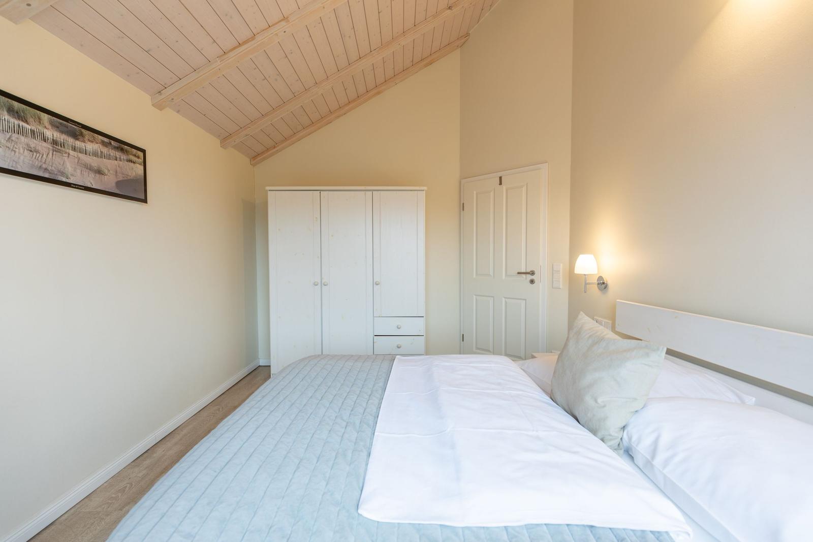 Schlafzimmer mit Doppelbett, Kleiderschrank und Holzdecke.