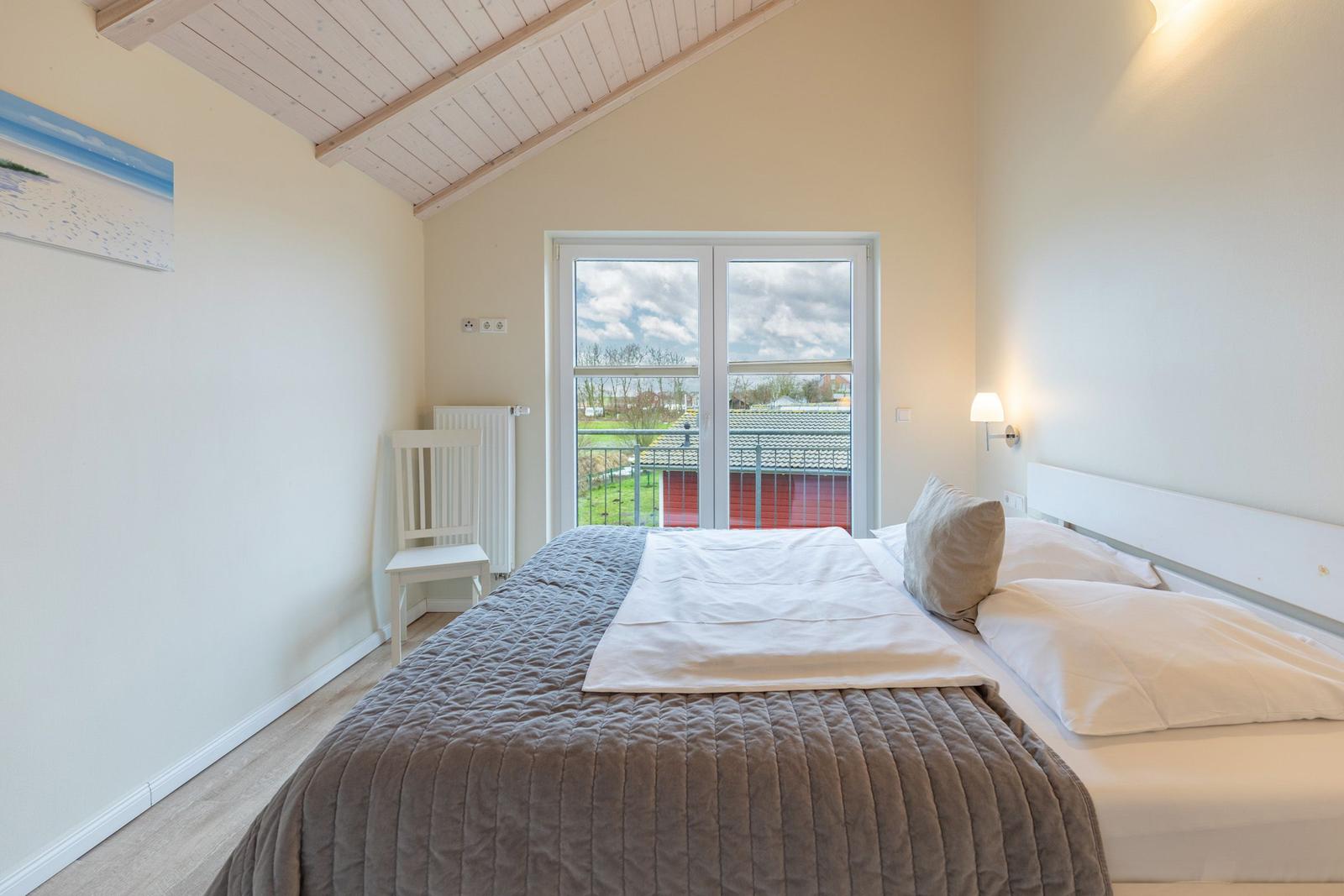 Schlafzimmer mit Bett, Fenster und Stuhl. Holzdecke und Wandbild.