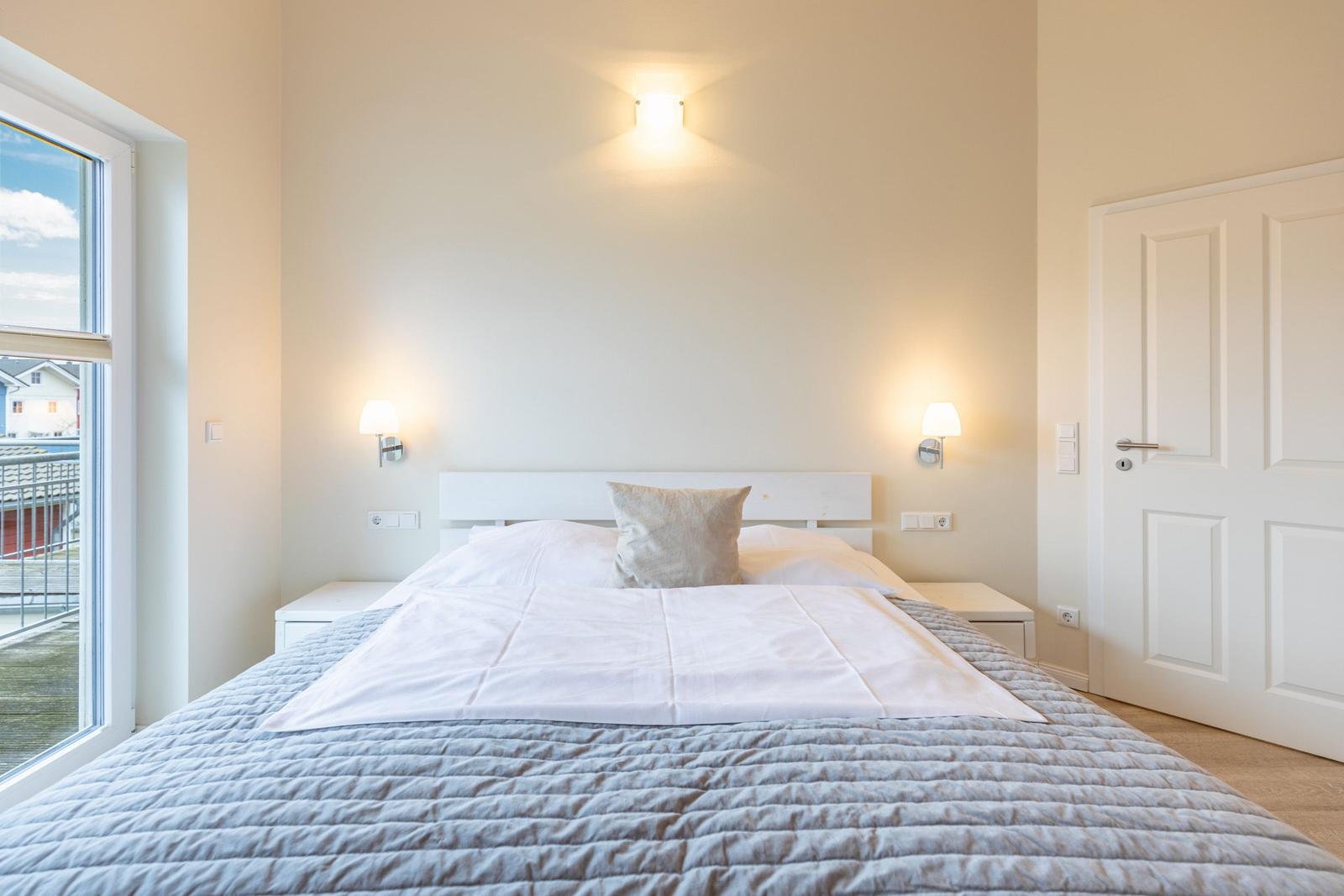 Schlafzimmer mit Bett, Nachttischen und Fenster. Weiße Wände und Beleuchtung.