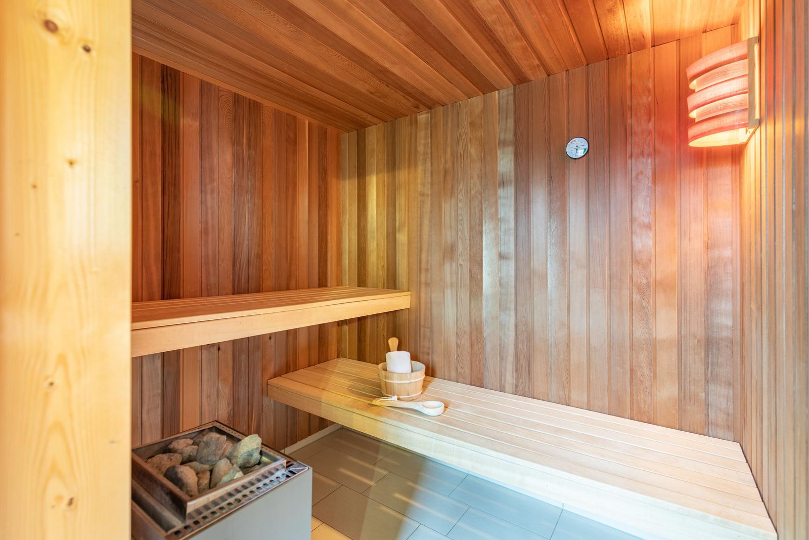 Sauna mit Holzwand, Bank, Steinkiste und Thermometer.