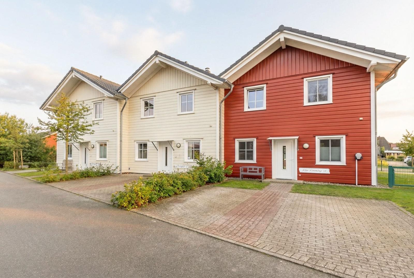 Rotes und cremefarbenes Ferienhaus mit gepflastertem Weg und grüner Umgebung.