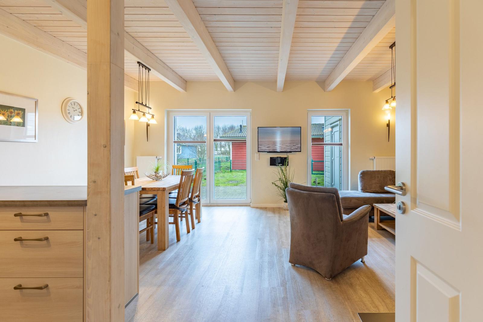 Wohn- und Essbereich mit Holzdecke, TV und Gartenblick.