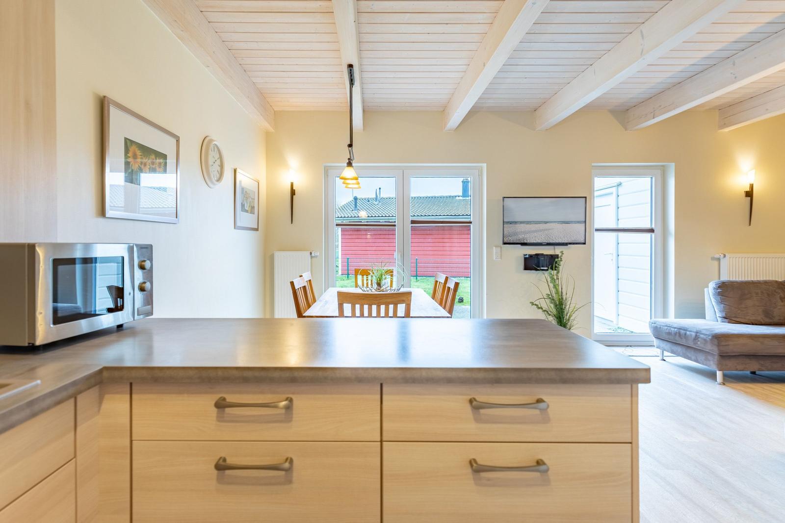 Küche mit Essbereich und Wohnzimmer mit Holzdecke und Fenstern.