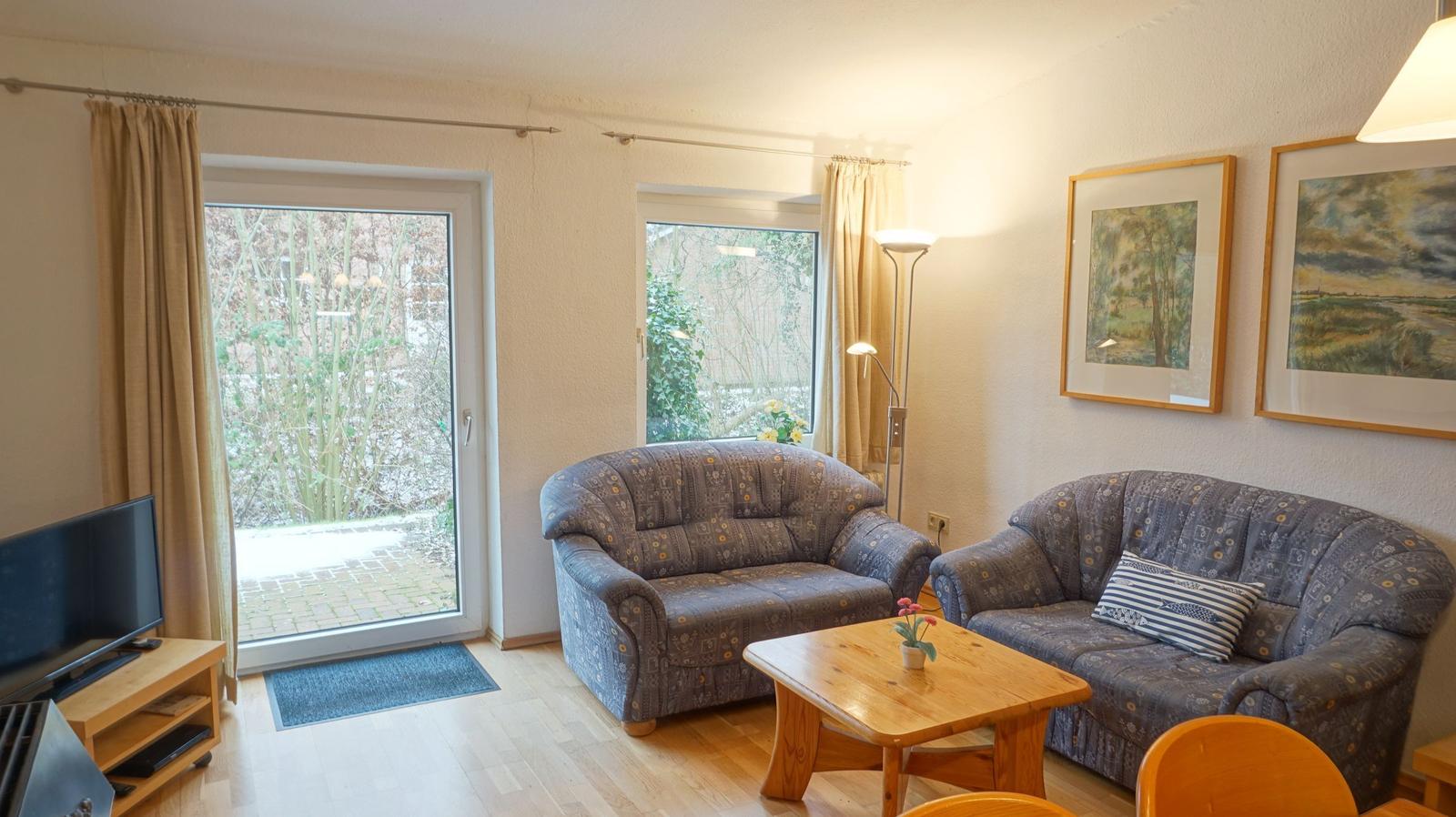 Wohnzimmer mit zwei Sofas, Holztisch und Fenstern zum Garten.