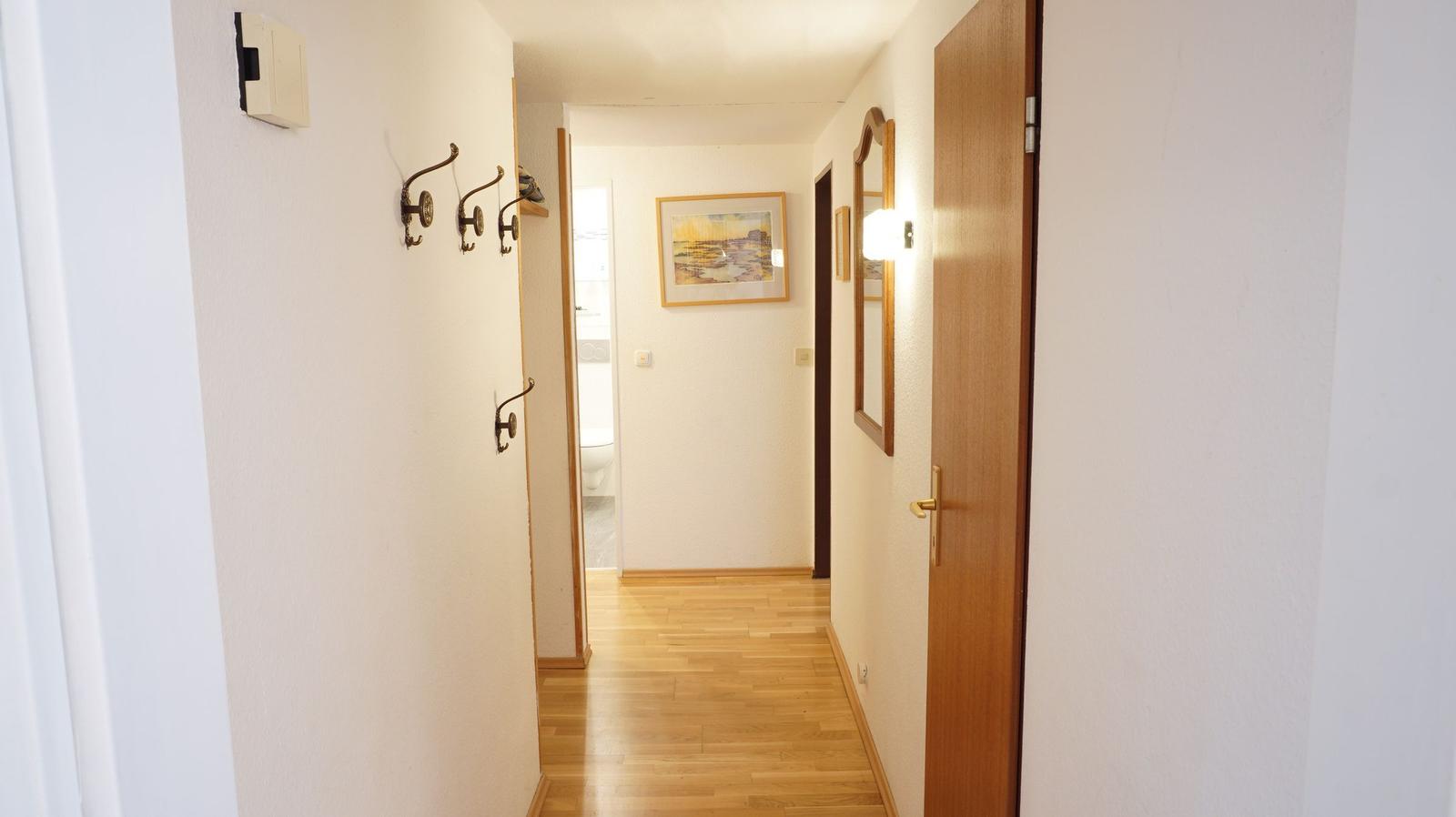 Flur mit Holzboden, Haken, Spiegel und Türen. Bild an der Wand.