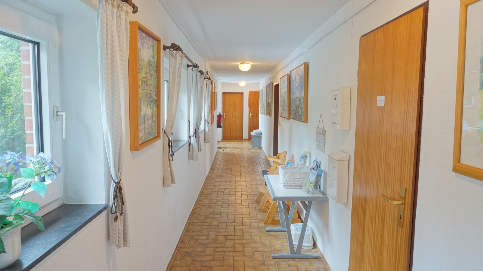 Flur mit Holztüren, Bildern und Fenster mit Pflanze.