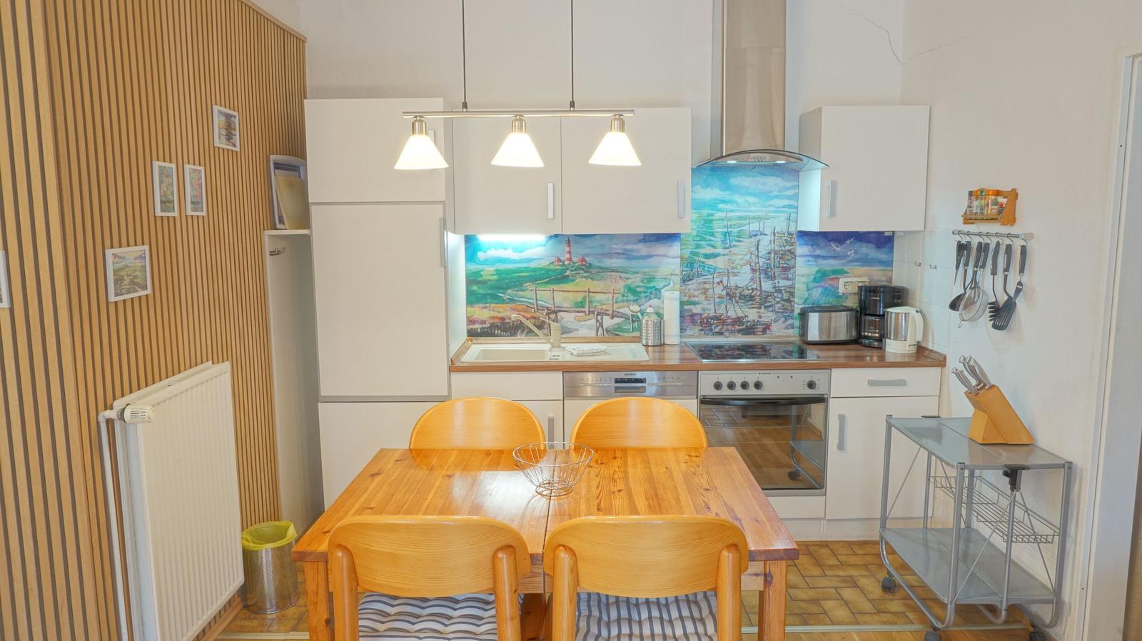 Küche mit Essbereich, Holztisch, weißen Schränken und farbigem Küchenrückwandbild.