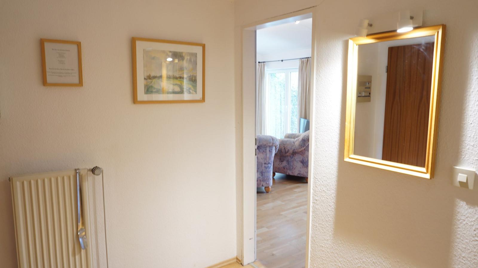 Flur mit Spiegel, Bildern und Blick in Wohnzimmer mit Sofa.