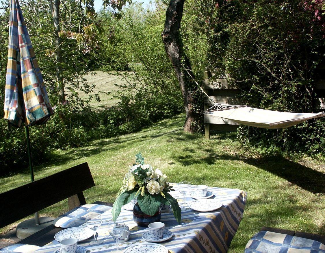 Garten mit gedecktem Tisch, Sonnenschirm und Hängematten unter Bäumen.