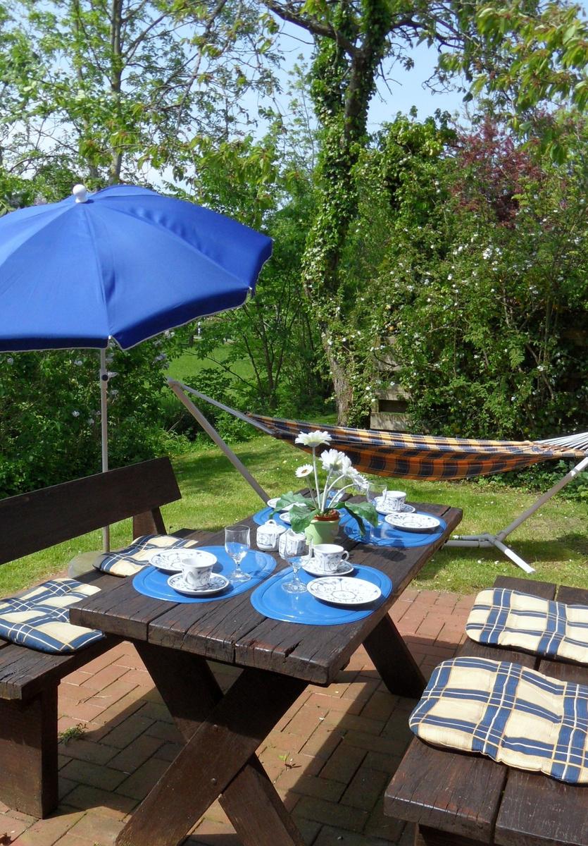 Holztisch mit blauer Sonnenschirm und Hängematten im Garten