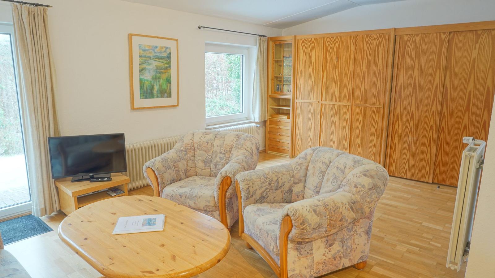 Wohnzimmer mit zwei Sesseln, Couchtisch und TV. Holzmöbel und Fenster zur Außenseite.