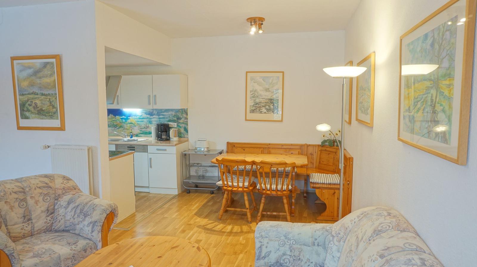 Wohnzimmer mit Essbereich und Küchenbereich. Holzmöbel und Wandbilder.