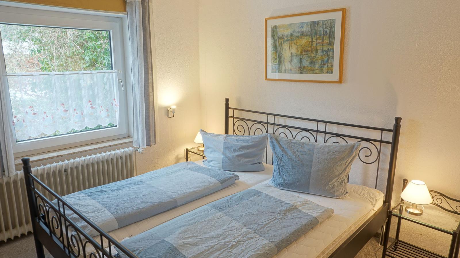 Schlafzimmer mit Doppelbett, Fenster und Nachttischen.