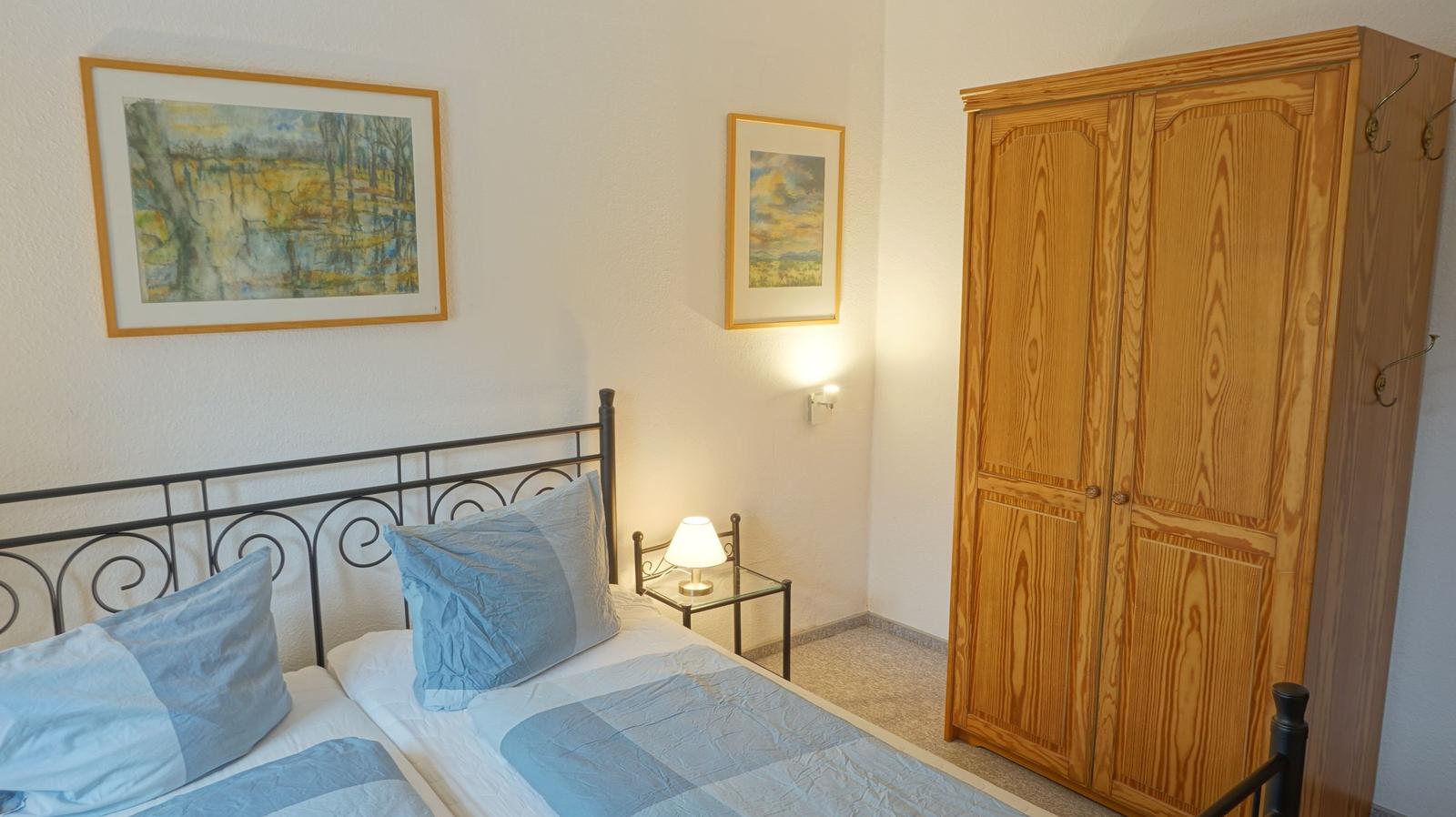 Schlafzimmer mit Bett, Kleiderschrank und Wandbildern.