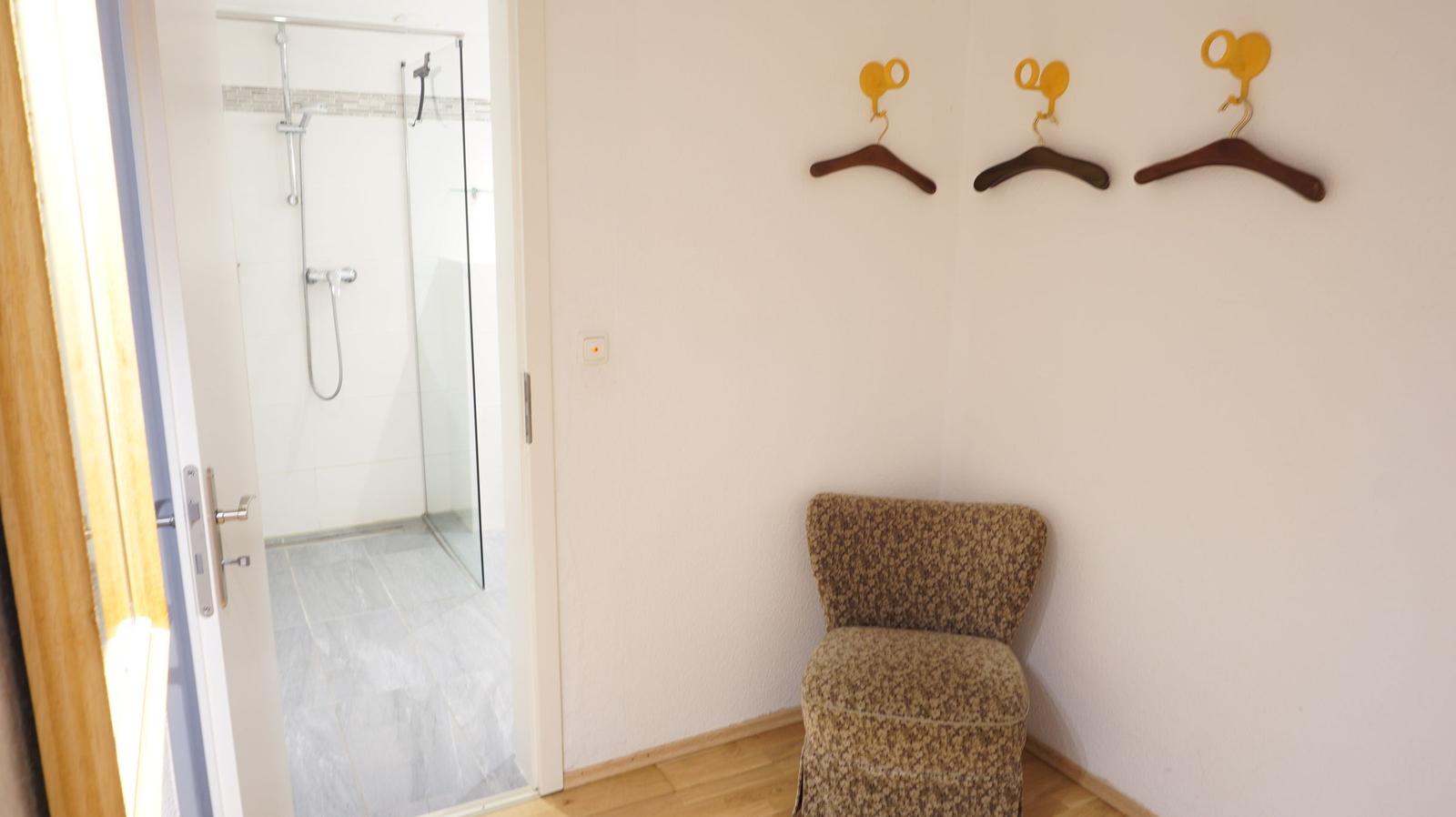 Flur mit Stuhl, Kleiderhaken und Blick in die Dusche.