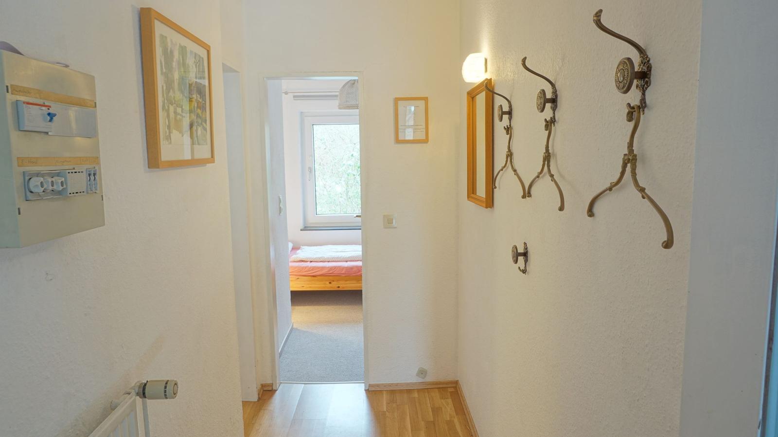 Flur mit Garderobe, Spiegel und Blick in Schlafzimmer mit Bett und Fenster.
