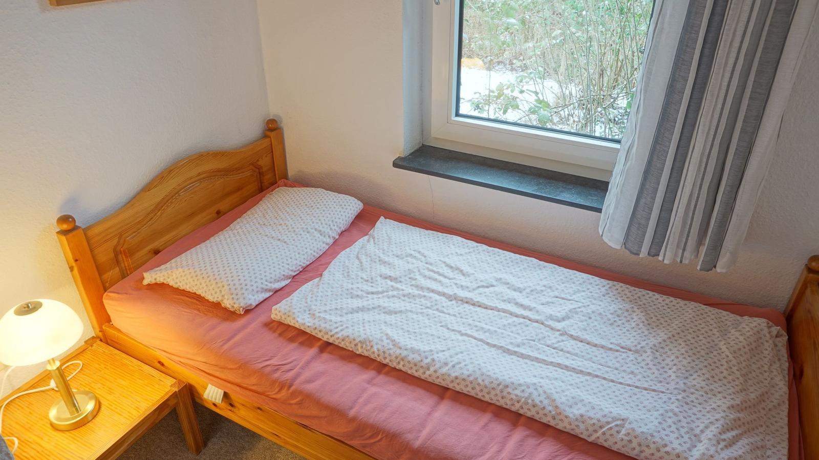 Ein Schlafzimmer mit Holzbett, Nachttisch und Lampe. Fenster mit Blick auf Schnee.