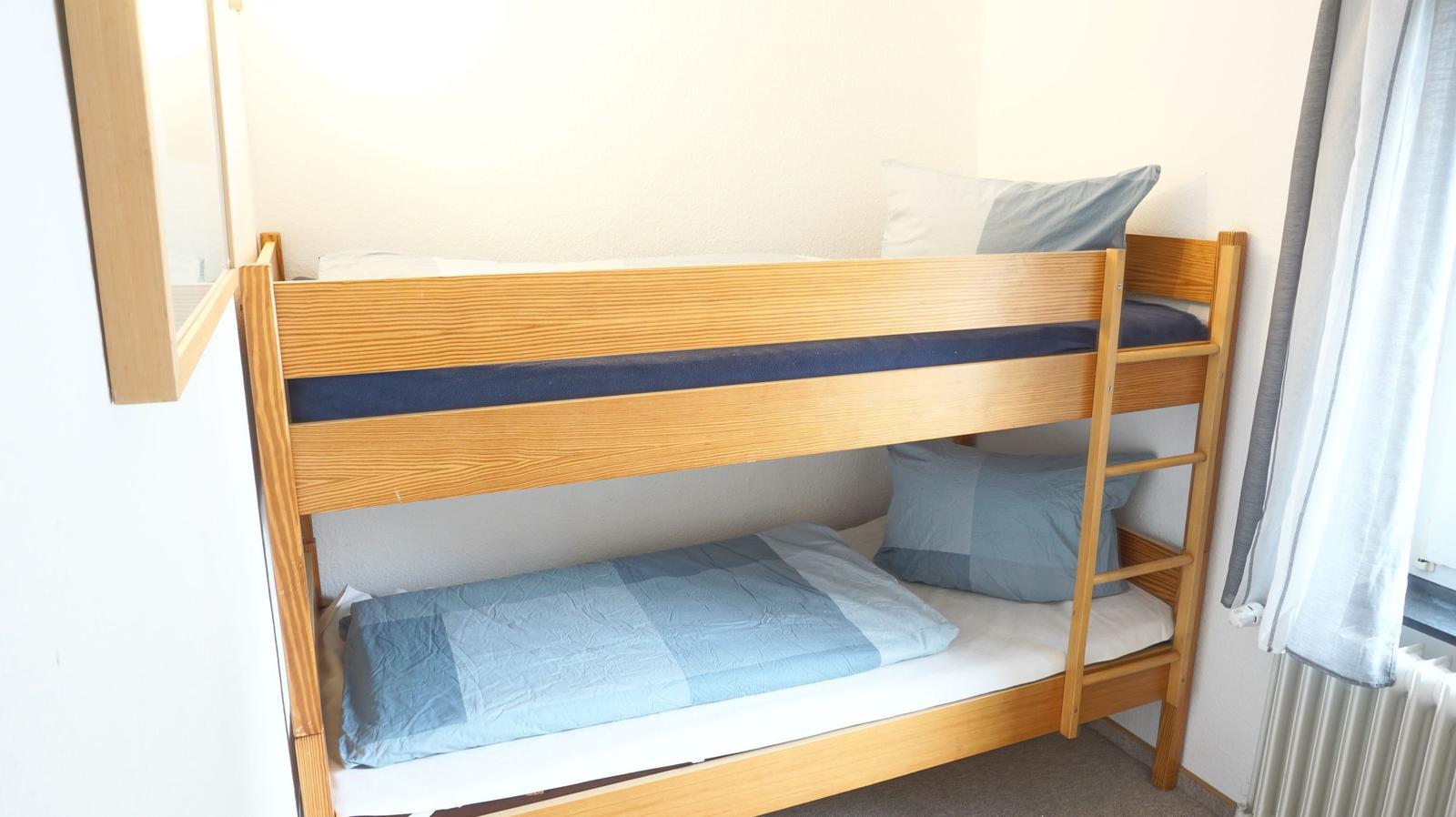 Ein Holz-Etagenbett mit blauen Bettwäsche und Kissen.