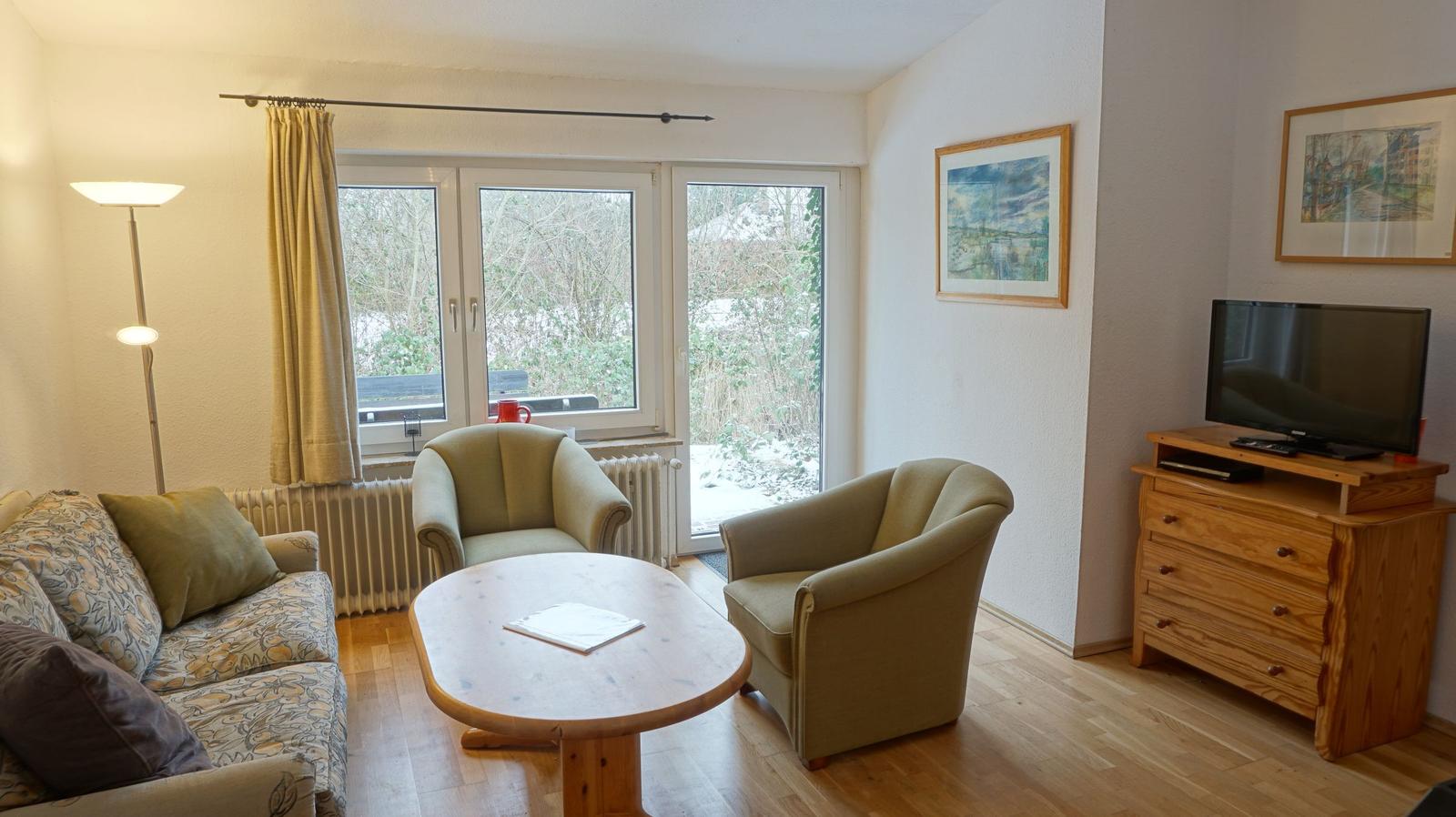 Wohnzimmer mit Sofa, zwei Sesseln, Tisch und Fernseher.