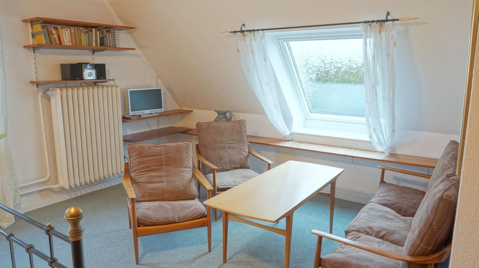 Wohnzimmer mit Sofa, zwei Sesseln, Tisch und Dachfenster.