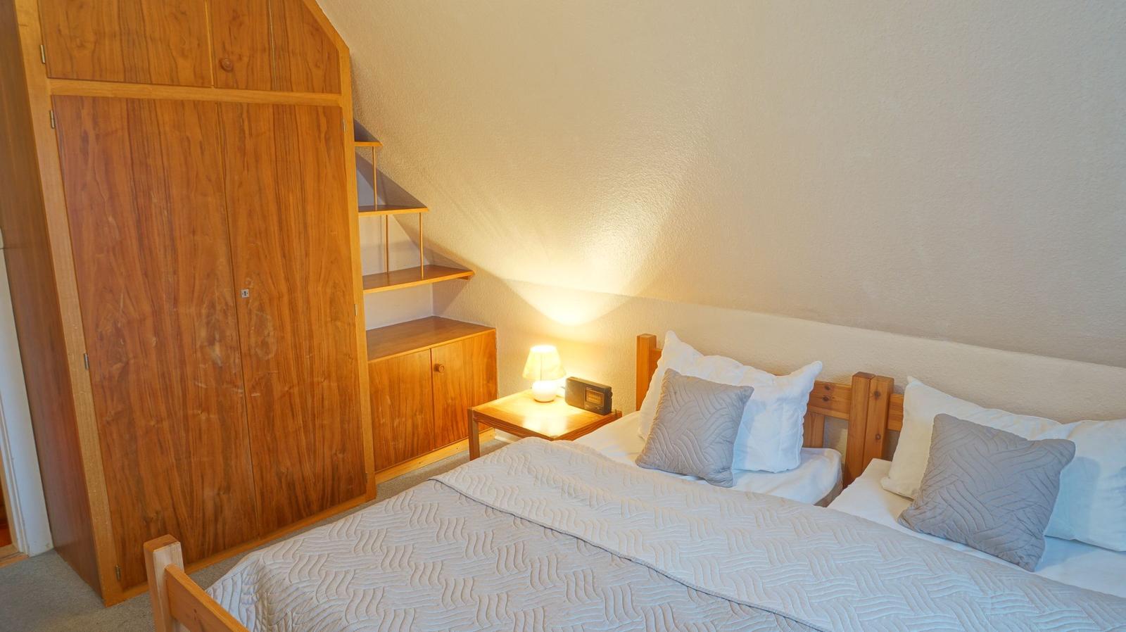 Schlafzimmer mit Doppelbett, Holzschrank und Nachttisch mit Lampe.