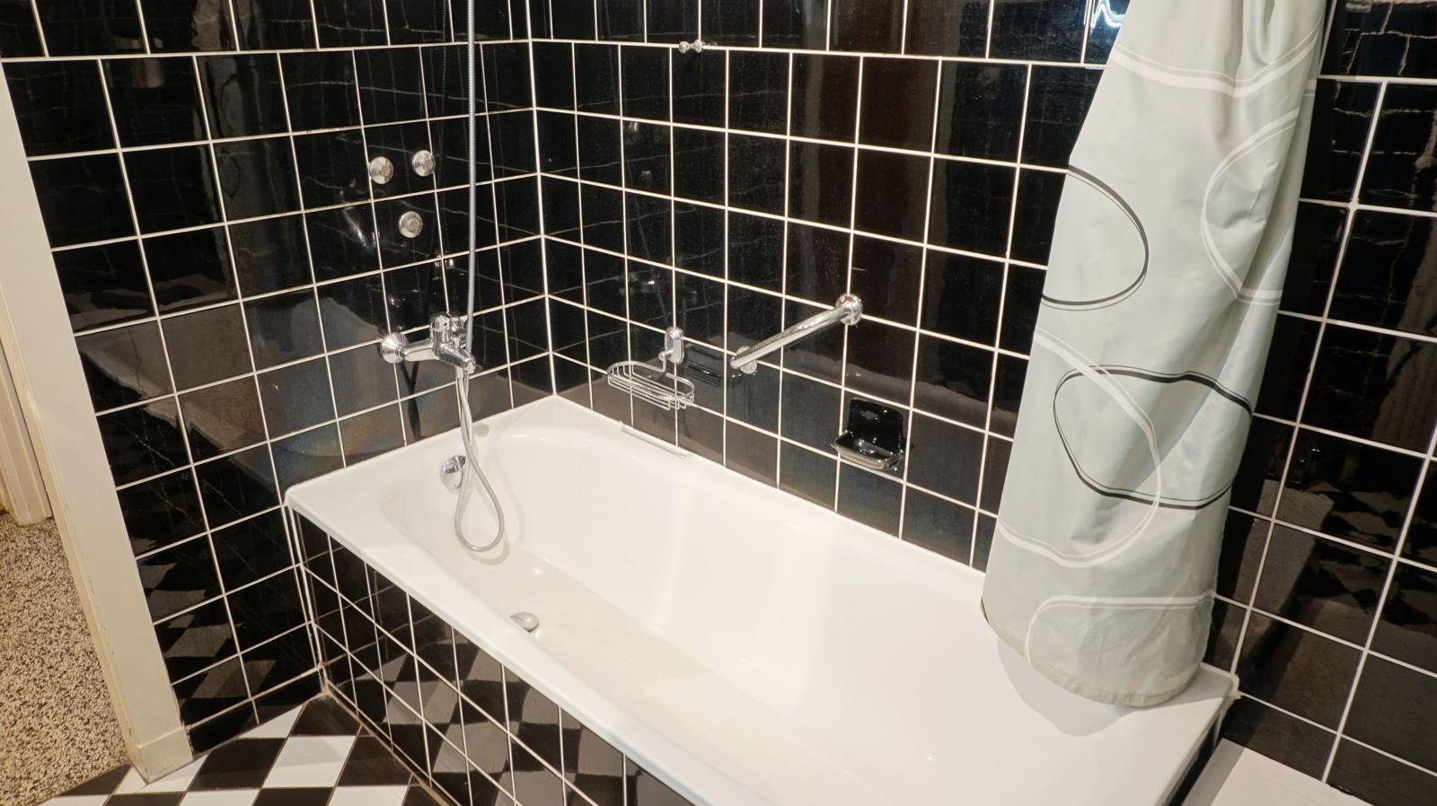 Bad mit weißem Badewannen-Set und schwarzen Fliesen an den Wänden.