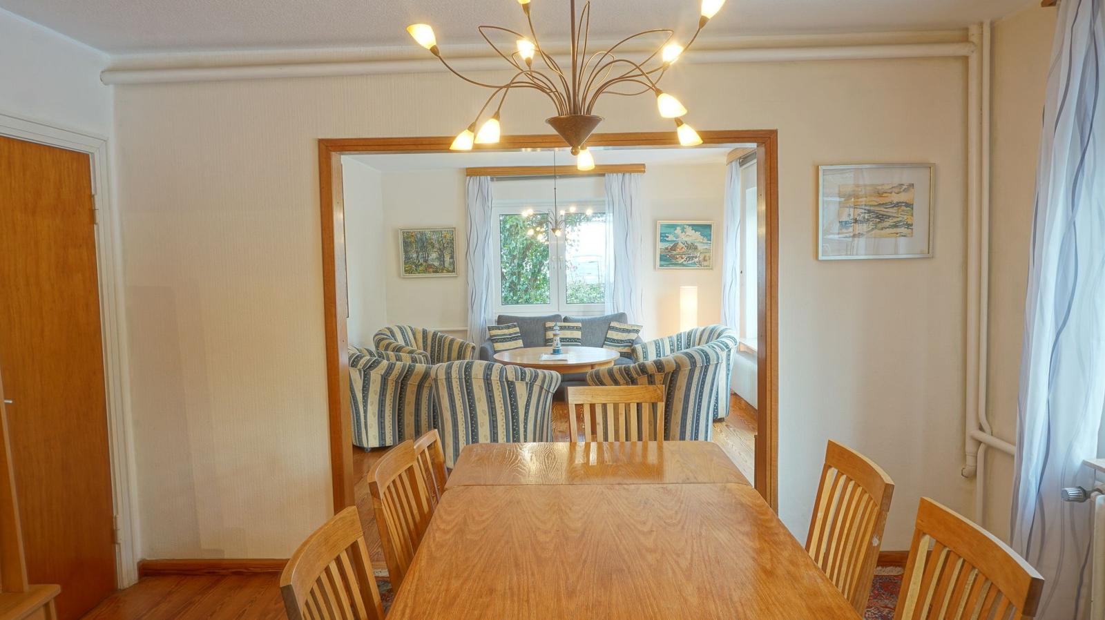 Esszimmer mit Holztisch und Stühlen. Durchgang in Wohnzimmer mit Sofa und Tisch.