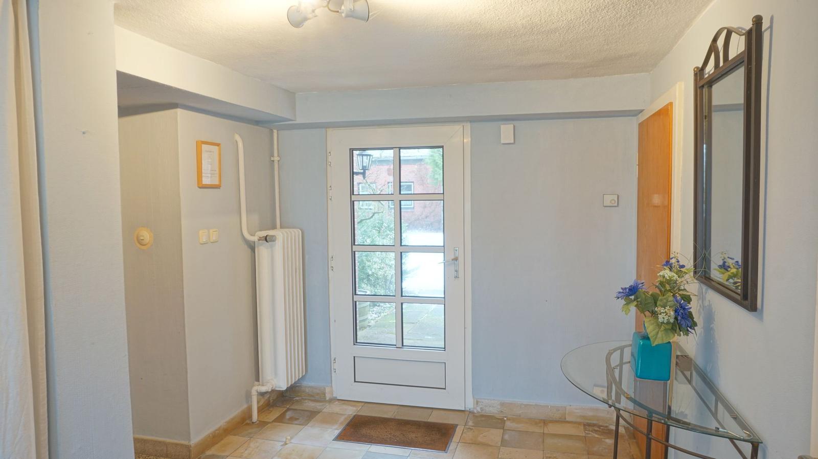 Eingangsbereich mit Glastür, Spiegel und Glas-Tisch mit Blumen.