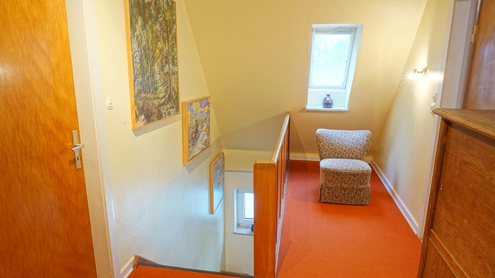 Flur mit Stuhl, Wandbildern und rotem Teppichboden